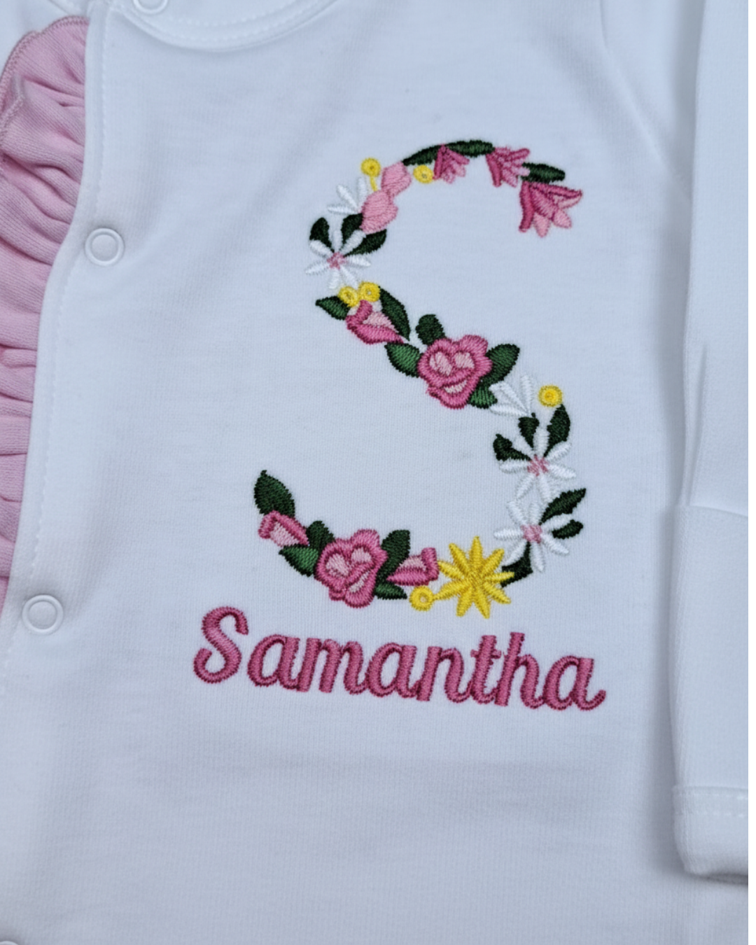 Close-up of embroidered floral initial and personalized baby name on baby girl sleep and play outfit