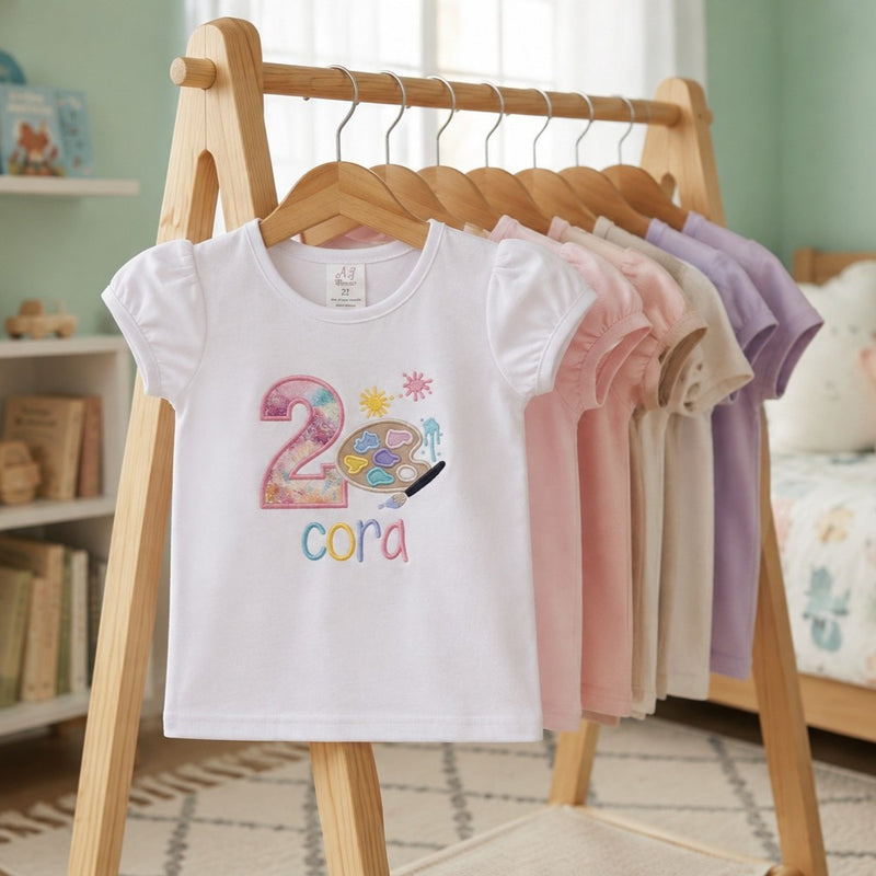 Children's t-shirts with colorful designs on a wooden rack in a room.