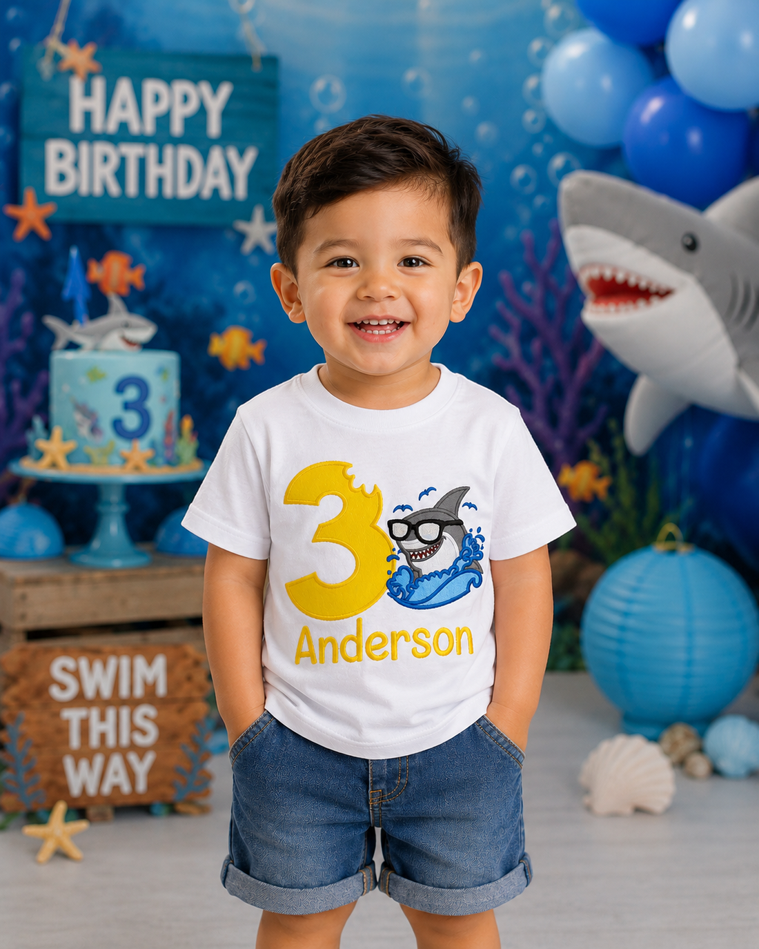 Personalized embroidered shark birthday shirt for boys featuring a cool shark wearing sunglasses, yellow number 3, and custom embroidered name Anderson on a white 100% cotton shirt at a shark-themed birthday party. | RoJo Custom Designs