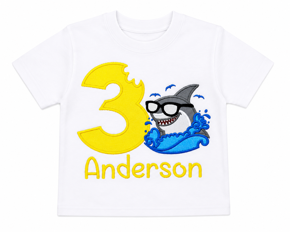 Lay-flat view of a personalized embroidered shark birthday shirt featuring a cool shark wearing sunglasses, yellow number 3, and custom embroidered name Anderson on a white 100% cotton shirt. | RoJo Custom Designs