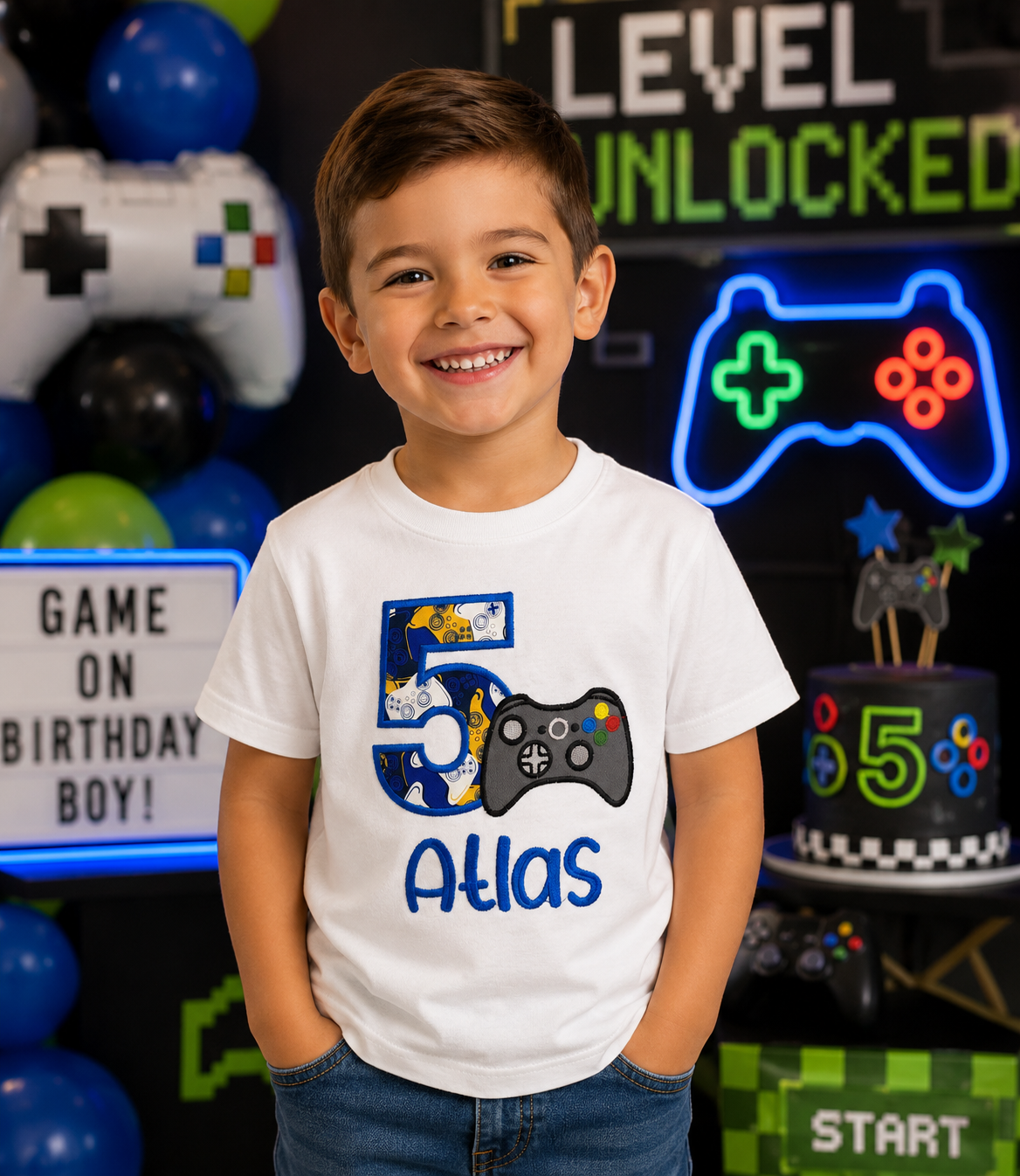 Personalized embroidered gaming birthday shirt for boys featuring a blue number 5, video game controller, and custom embroidered name Atlas on a white 100% cotton shirt displayed at a video game themed birthday party. | RoJo Custom Designs