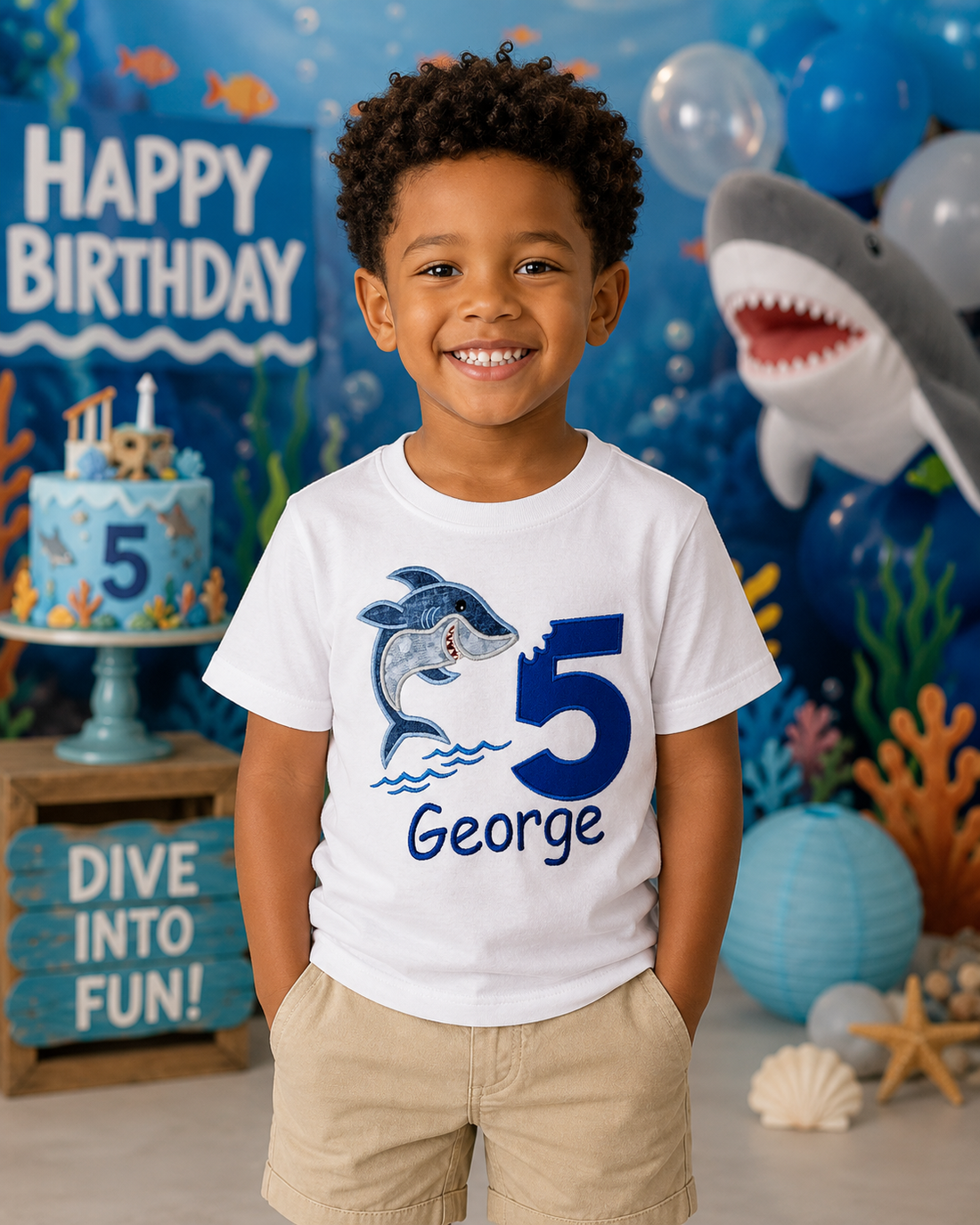 Personalized embroidered jumping shark birthday shirt for boys featuring a blue number 5, embroidered jumping shark, and custom embroidered name George on a white 100% cotton shirt at an ocean-themed birthday party. | RoJo Custom Designs