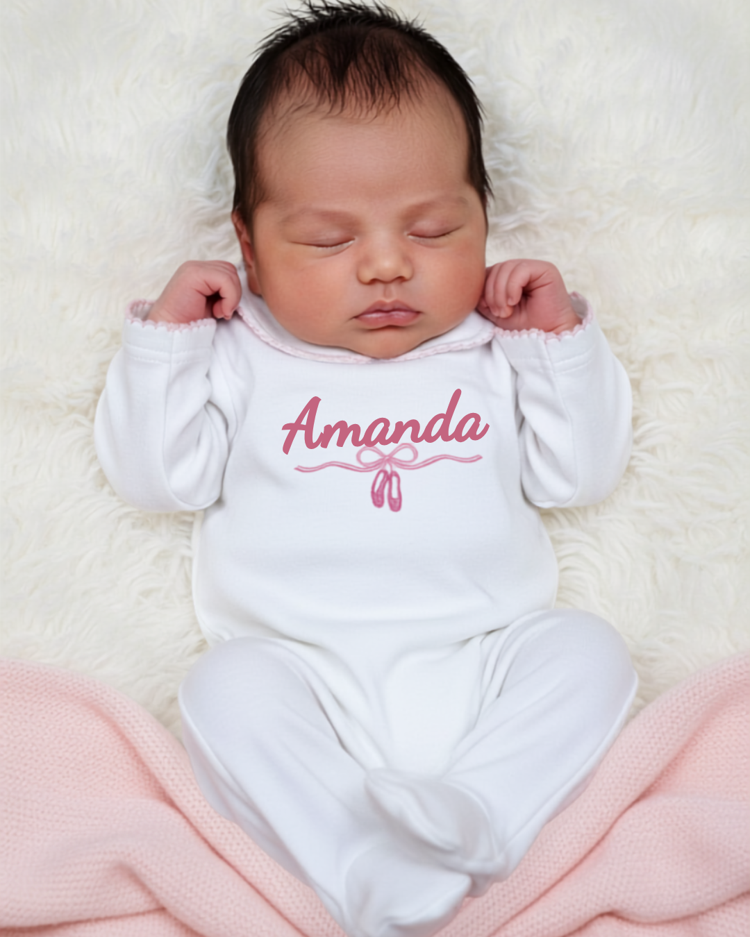 Newborn baby wearing a white onesie with 'Amanda' printed in pink on a soft white background.