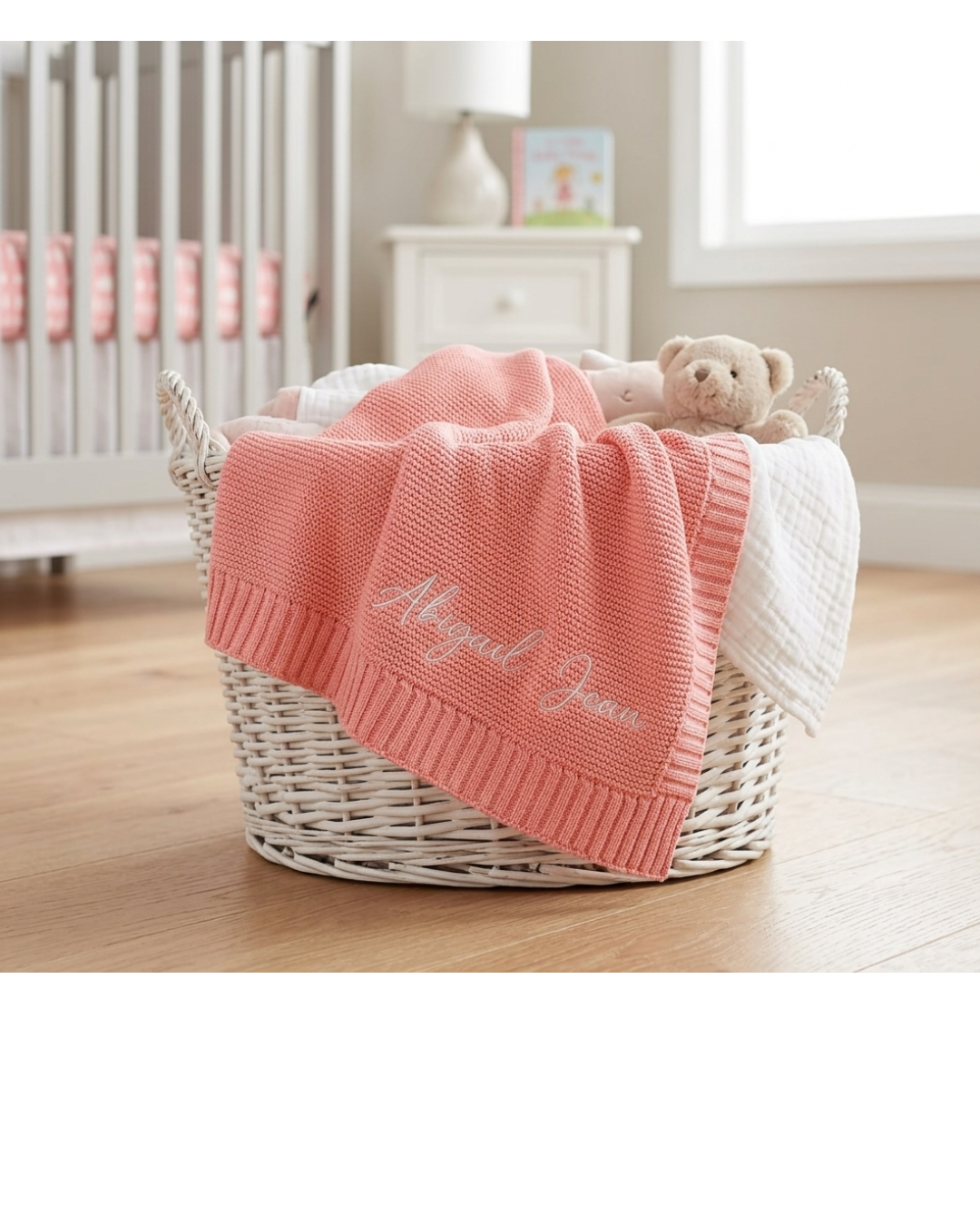 Pink personalized knit baby blanket embroidered with baby's name draped over nursery basket