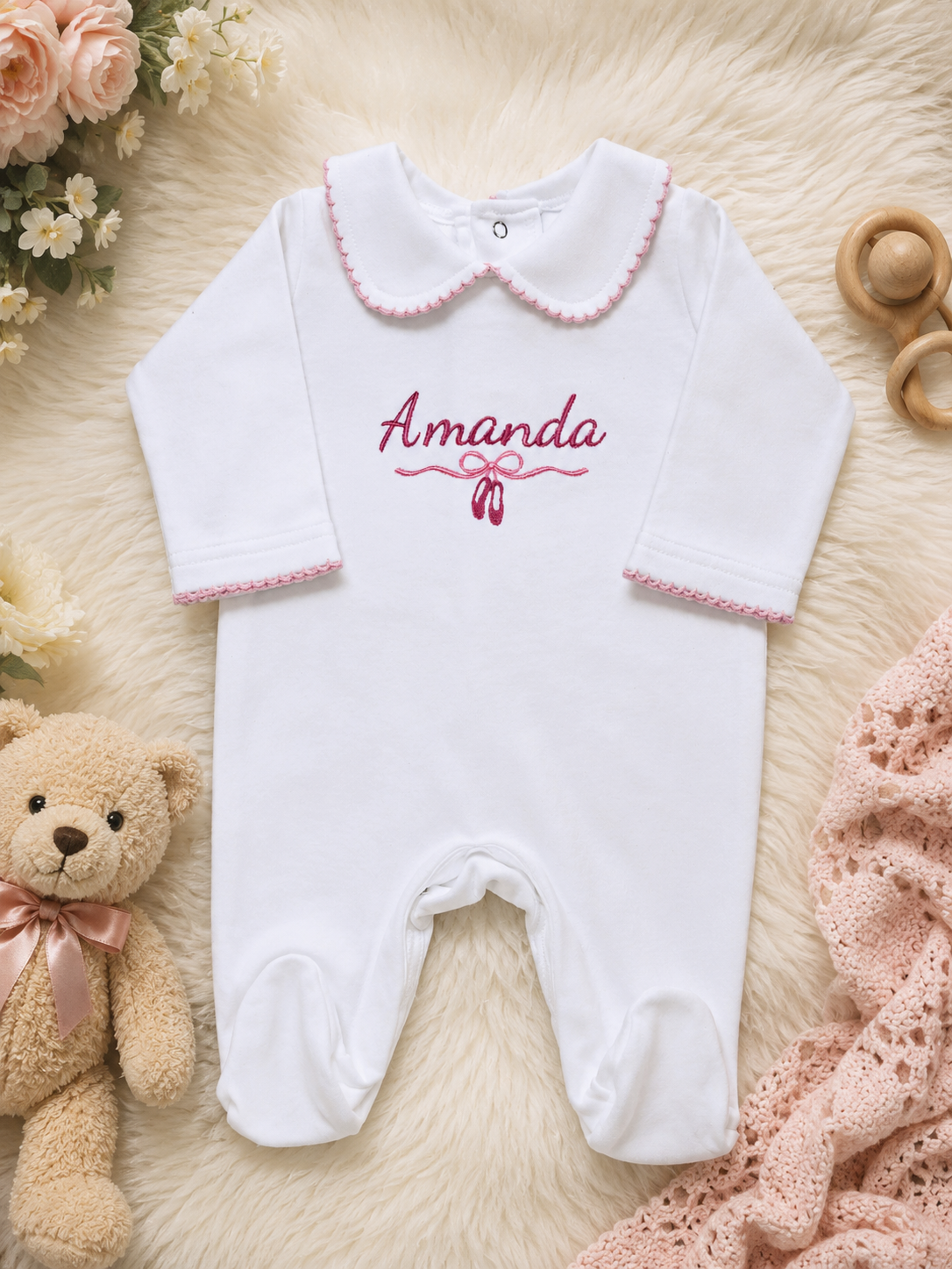 Newborn baby wearing a white onesie with 'Amanda' printed in pink on a soft white background.